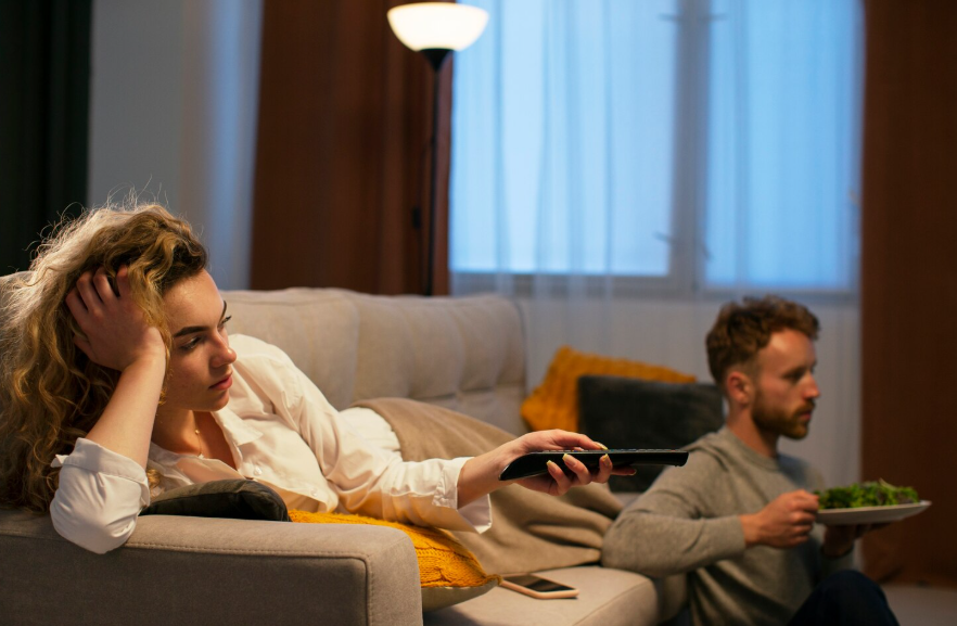 Couple experiencing streaming burnout while choosing what to watch in a living room.