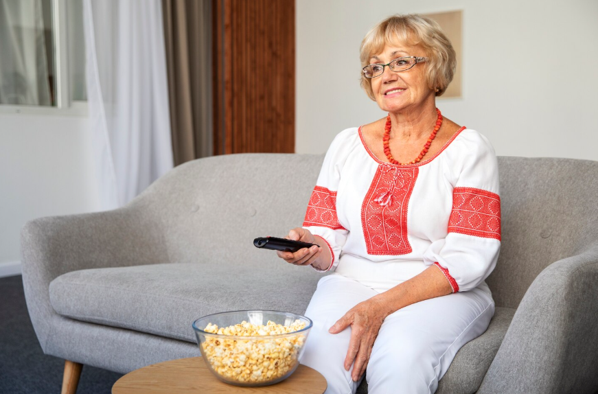 Senior watching TV with a remote illustrating cord-cutting for seniors to simplify home streaming.
