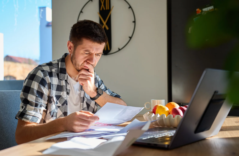 Man reviewing bills beside a laptop to calculate the true cost of cord-cutting.